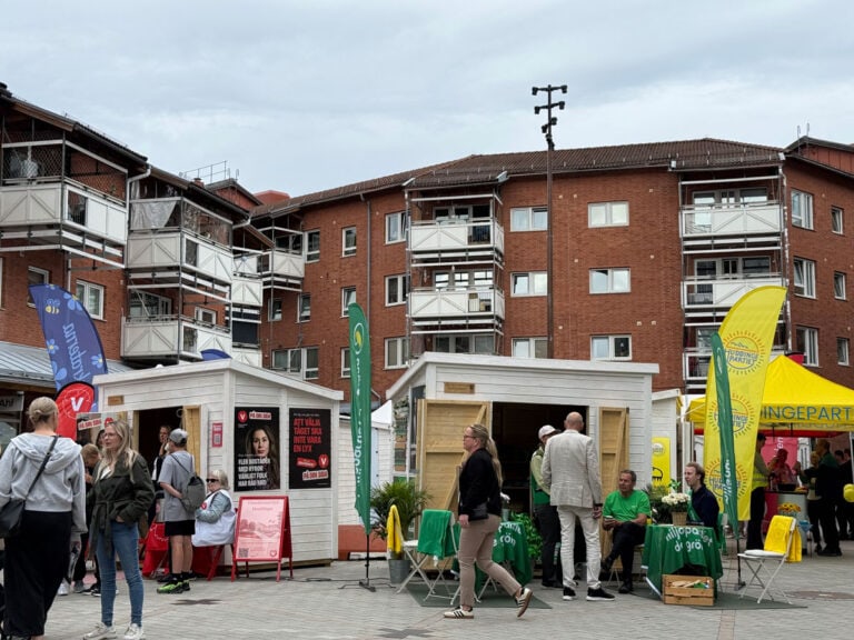 Valstugor från flera politiska partier på Sjödalstorget i Huddinge, med människor som rör sig på torget.